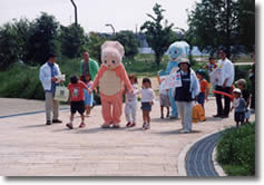 着ぐるみと一緒に公園を歩く子どもたちの写真